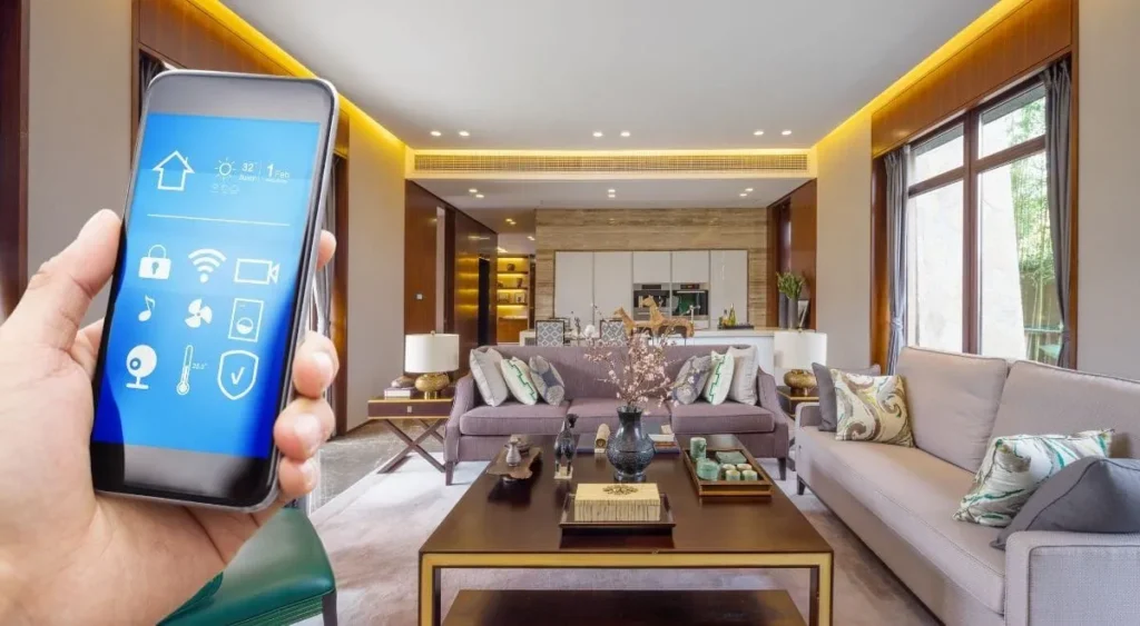 Hand holding a smartphone with a smart home control app displaying security, lighting, and temperature icons, set against an elegant living room background