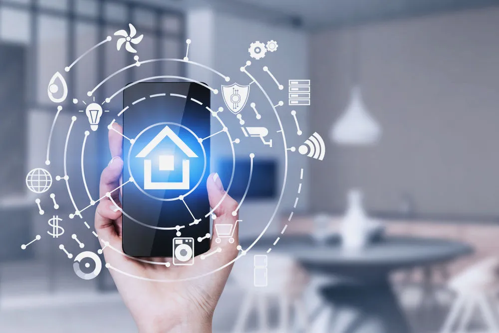 Hand holding a smartphone with a glowing smart home icon, encircled by connected icons representing IoT devices, security, and home automation features.